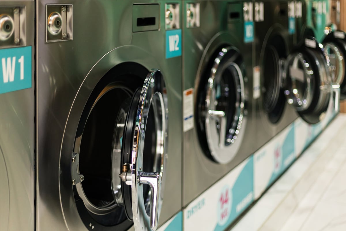 A row of stainless-steel commercial washing machines lining the wall of a laundry facility